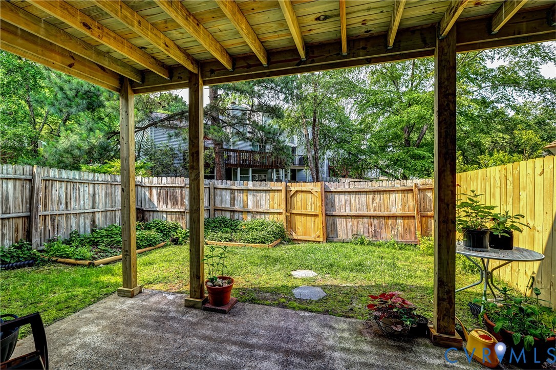 Covered wooden patio overlooking a fenced backyard with a lawn and garden beds.