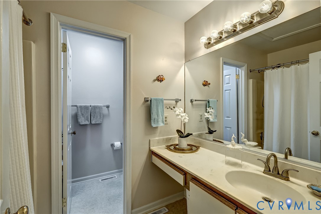 Bathroom with a long vanity, sink, large mirror, and shower behind a curtain.