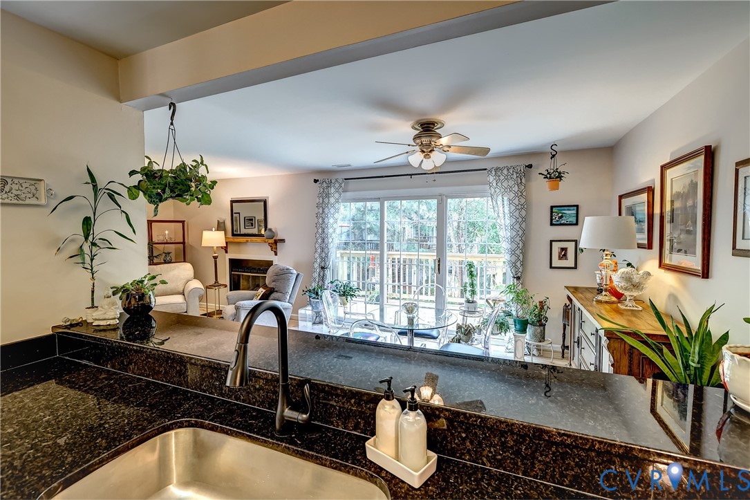 Kitchen with a granite island sink overlooking a furnished living area and deck through sliding glass doors.