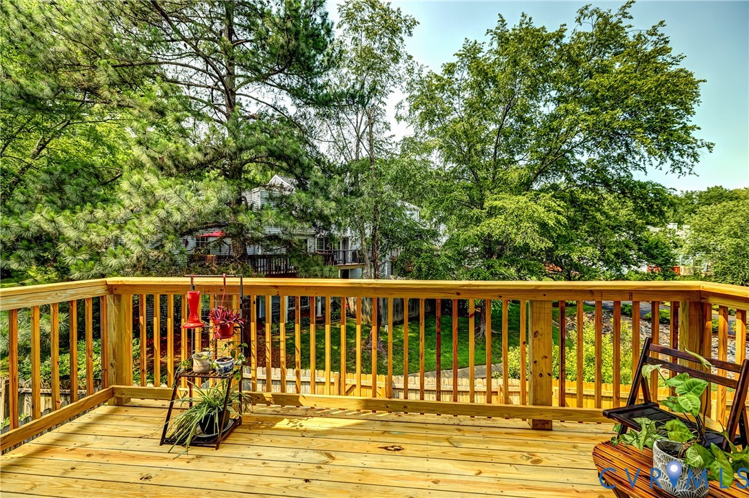 Wooden backyard deck with potted plants and a chair, overlooking leafy trees and neighboring homes.