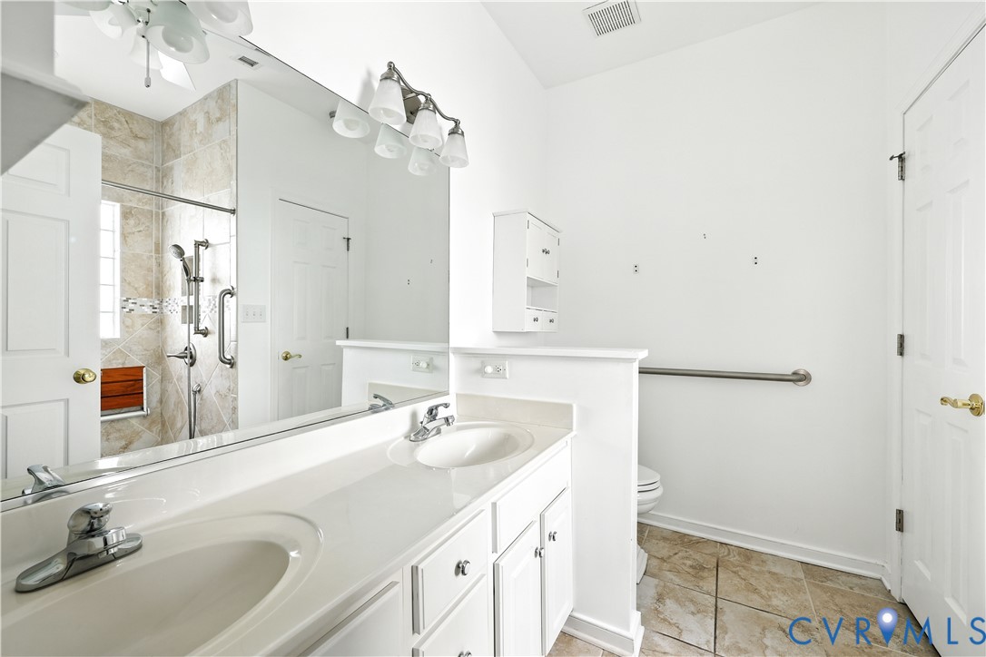 Bathroom with a long double-sink vanity, large mirror, and tiled shower with a wooden bench.