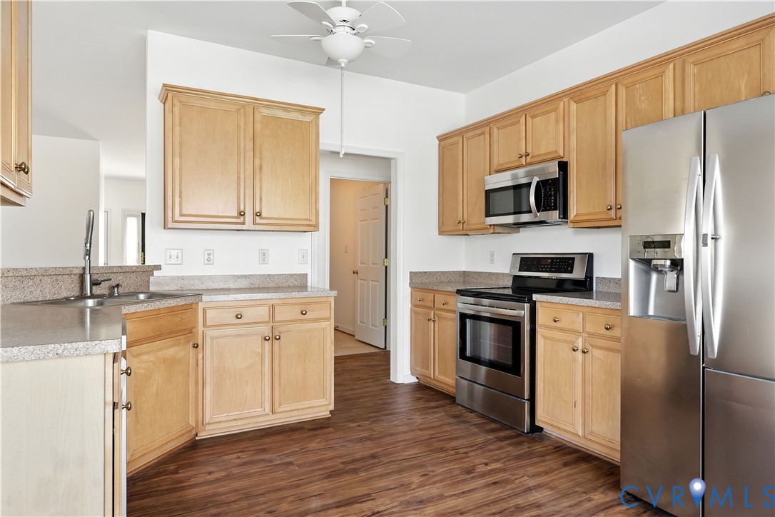 Kitchen with light wood cabinets, stainless steel appliances, and dark wood flooring.