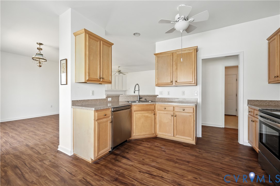Kitchen with light wood cabinets, speckled counters, stainless-steel appliances, and dark wood-look flooring.