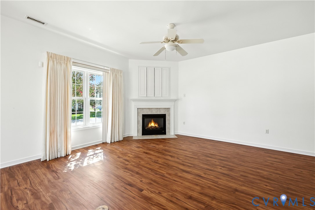 Empty living room with wood floors, a fireplace, and a large curtained window.