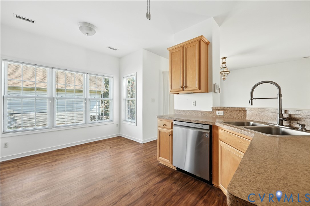 Vacant kitchen with wood cabinets, a stainless steel dishwasher, and large windows.