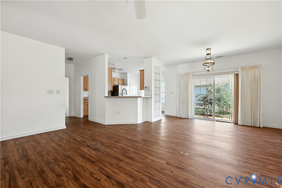 Vacant living room with dark wood floors, open kitchen, and sliding glass doors to a patio.