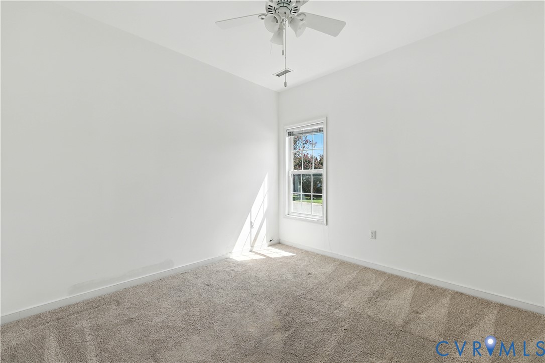 Empty bedroom with beige carpet, a ceiling fan, and a sunlit window.