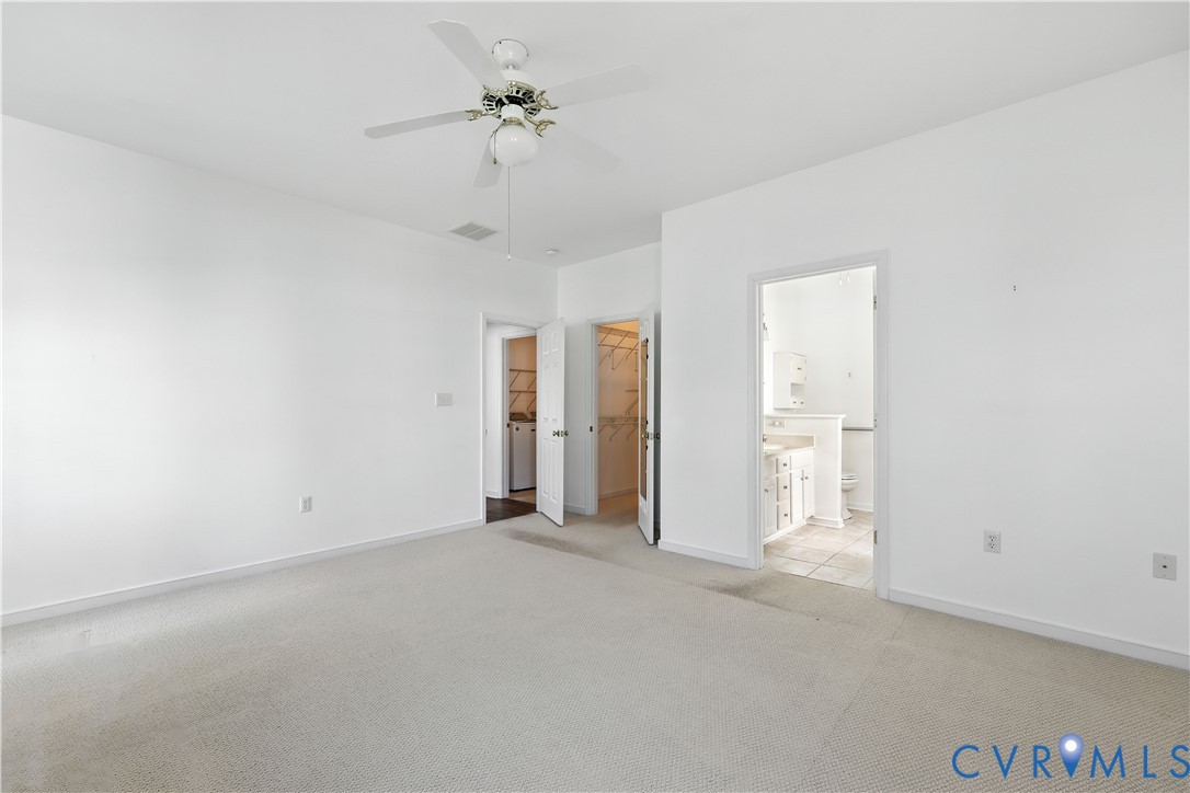 Empty carpeted bedroom with a ceiling fan, two open closets, and an adjoining bathroom.