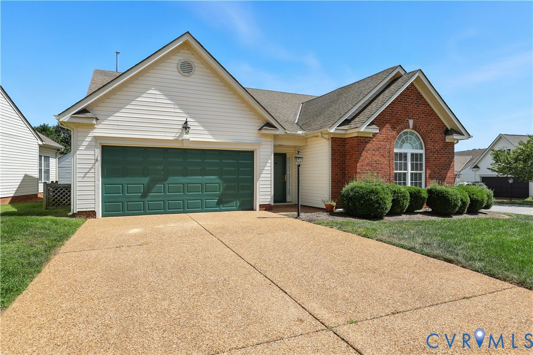 Home with a red brick gable, arched window, green double garage door, and wide driveway.