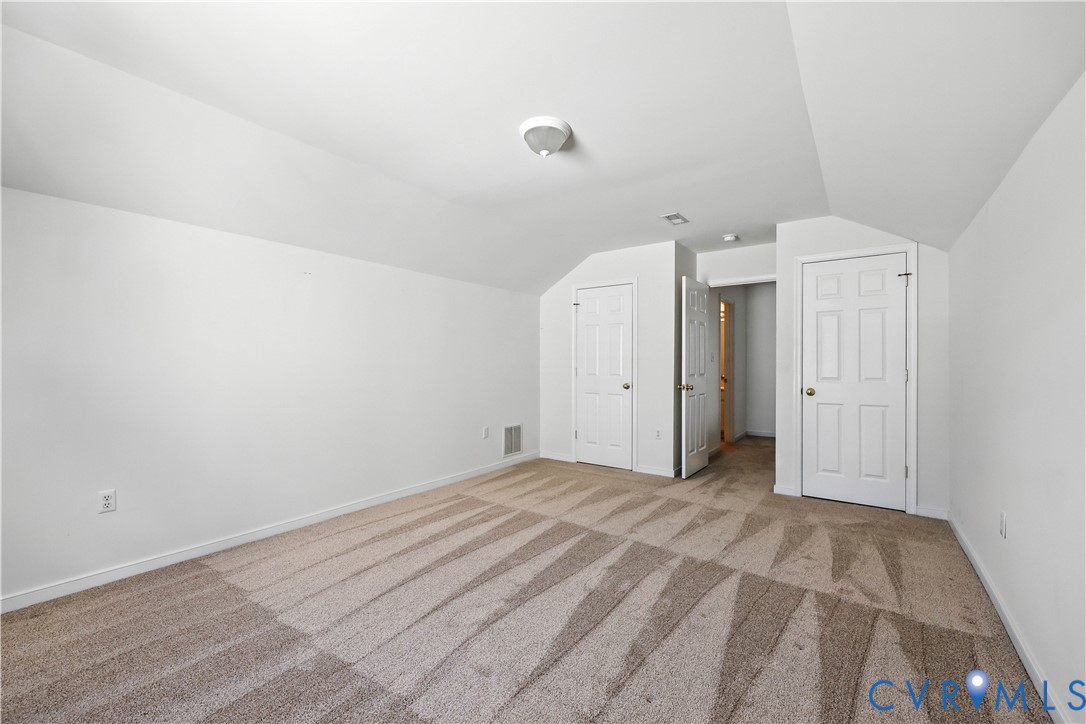 Empty carpeted bedroom with a sloped ceiling and multiple white doors.