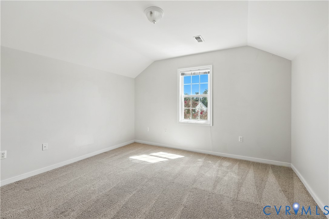 Empty carpeted bedroom with a vaulted ceiling and a sunlit window.