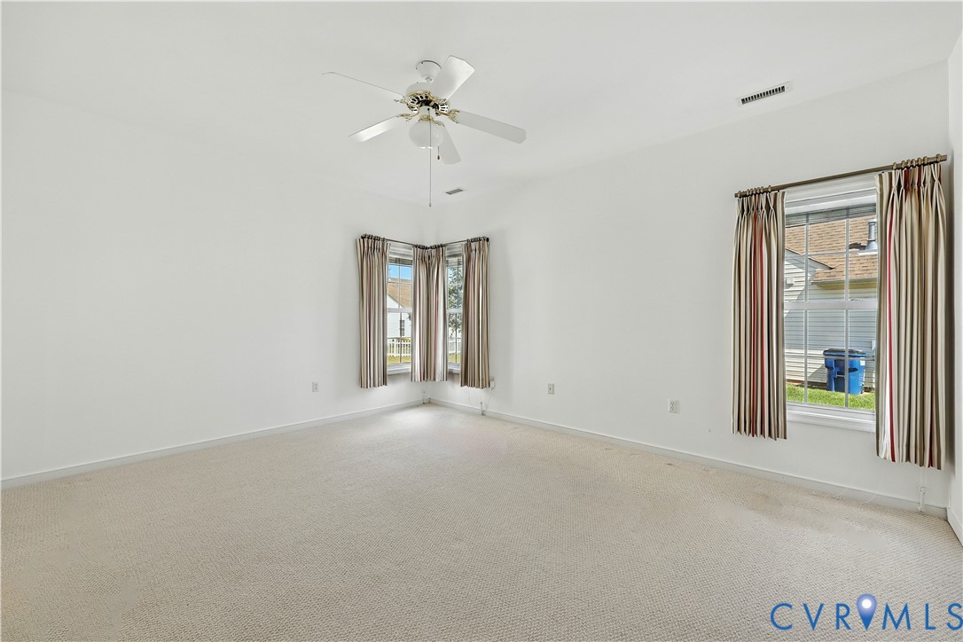 Empty carpeted room with a ceiling fan and two curtained windows.