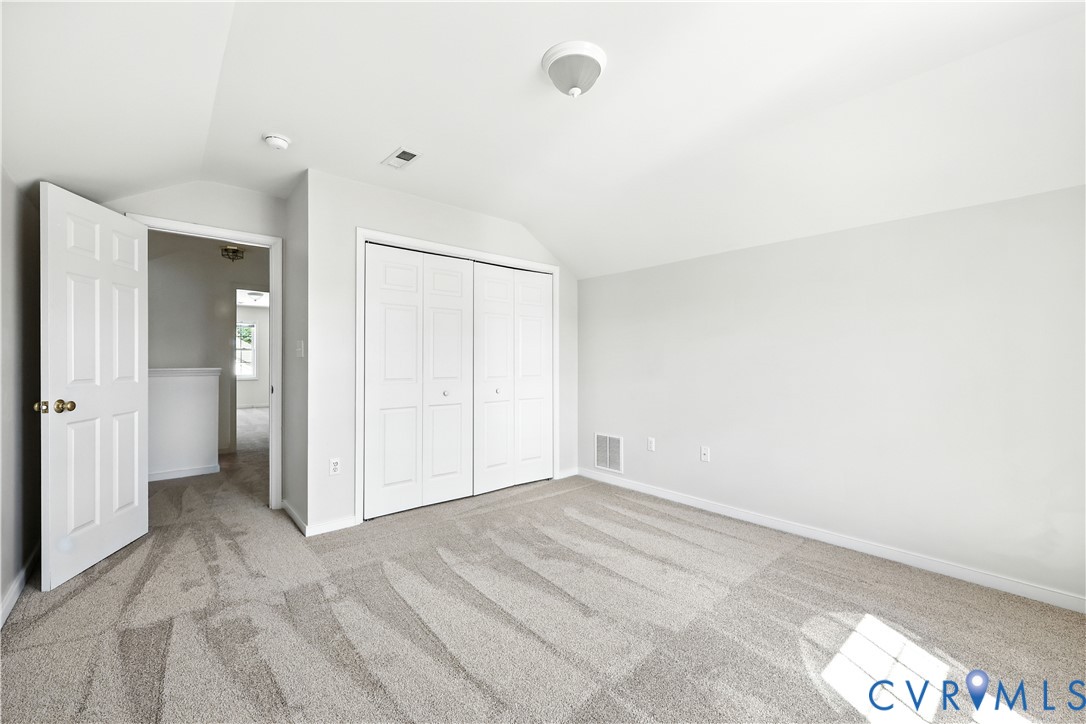Empty bedroom with gray carpet, double closet doors, and an open door to the hallway.