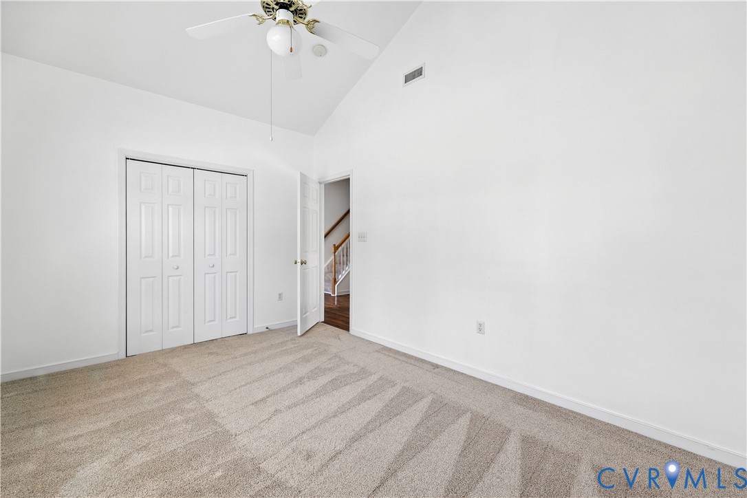 Empty bedroom with vaulted ceiling, beige carpet, and an open doorway to the staircase.