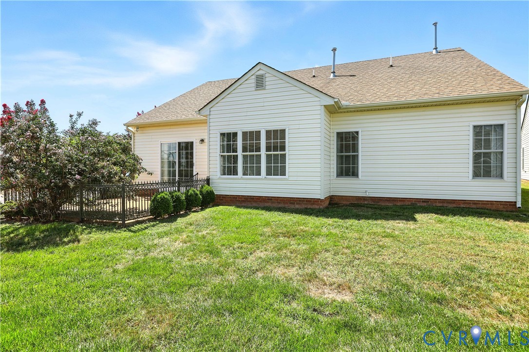 Rear of a light-colored house with a fenced patio and broad lawn.