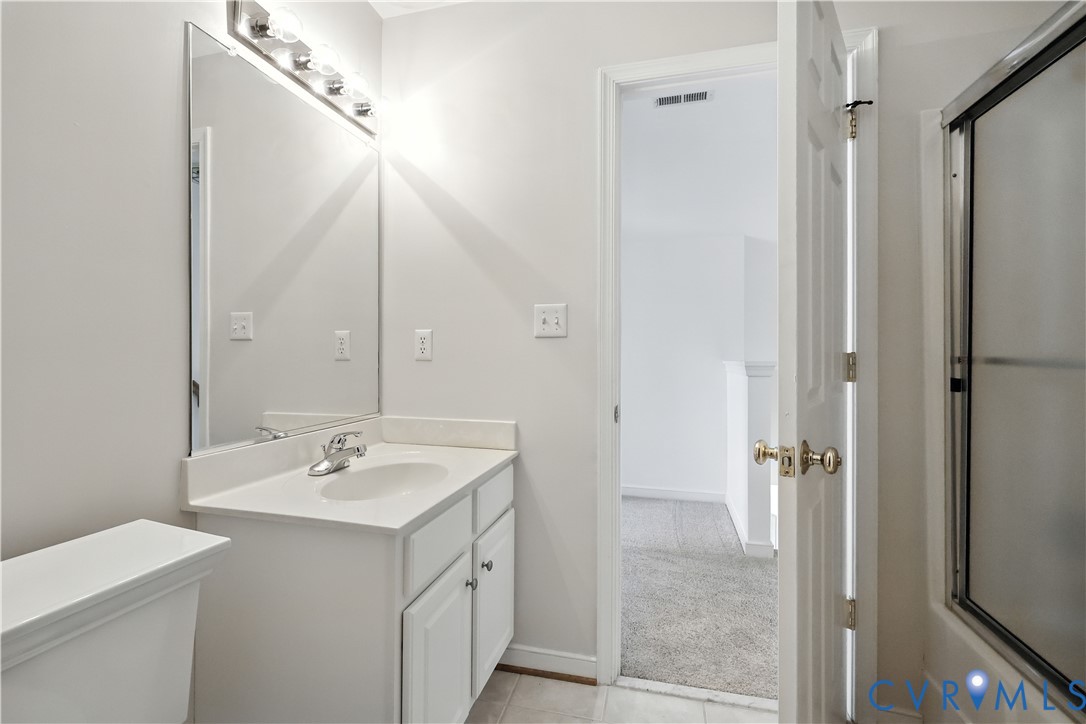 Bathroom with a white vanity and mirror, toilet, and glass-enclosed shower.