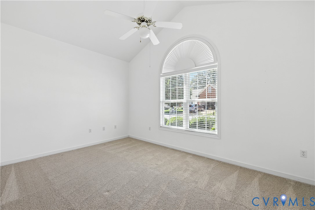 Empty carpeted bedroom with a ceiling fan and a large arched window with blinds.