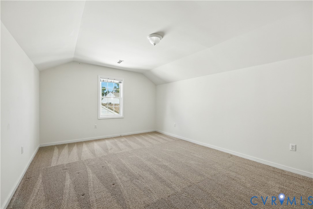 Empty carpeted room with a sloped ceiling and a single window.