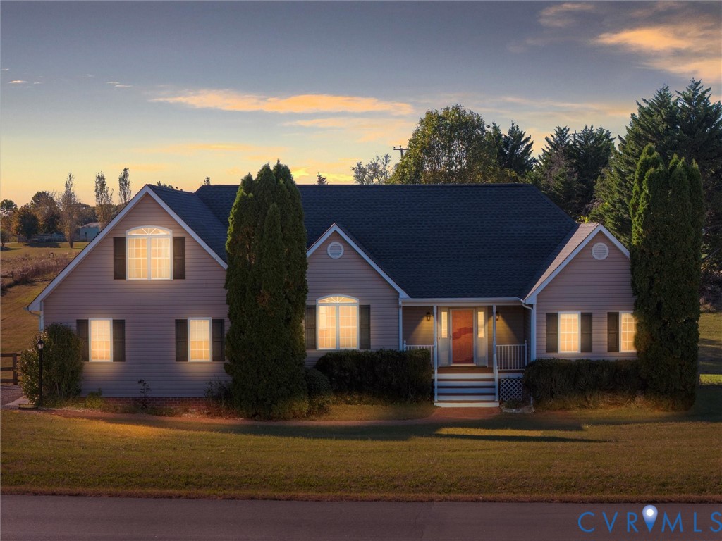 Home exterior at dusk with a covered entry, glowing windows, and a broad front lawn.