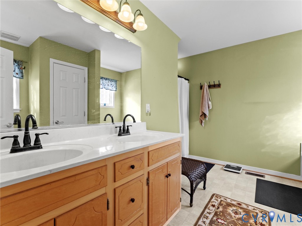 Bathroom with a double-sink vanity, honey-colored cabinets, and pale green walls.