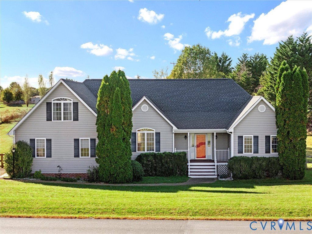 Gray home with a red front door, black shutters, and tall evergreens beside the lawn.