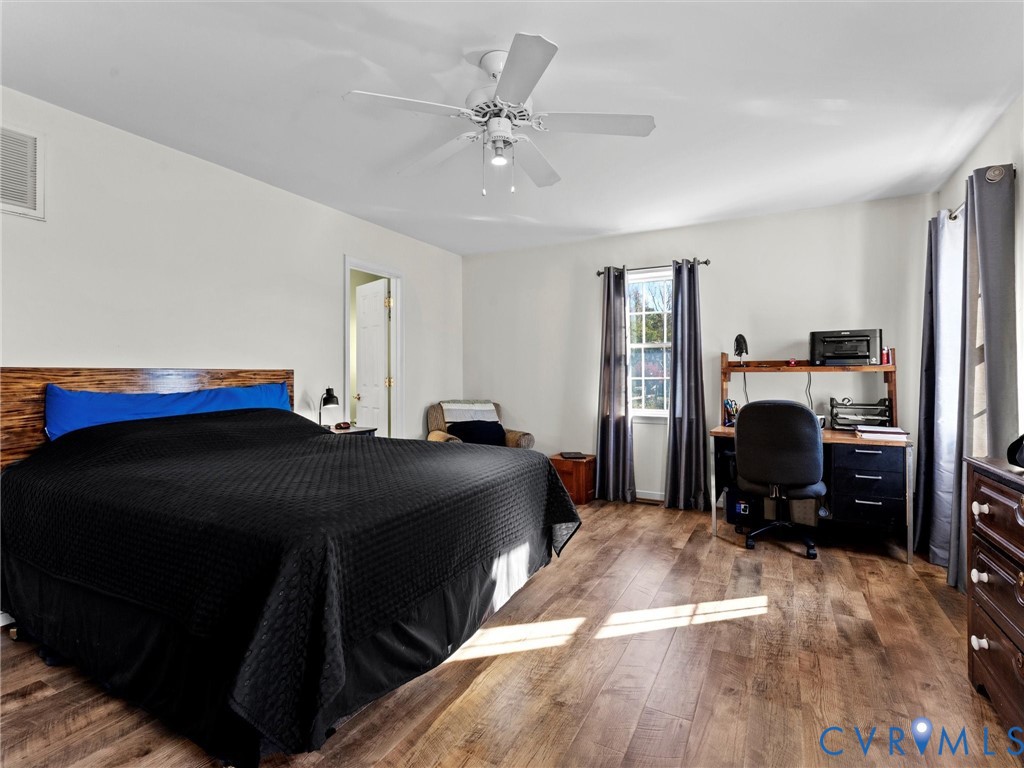 Bedroom with a black bedspread, wood-look flooring, and a desk beside the window.