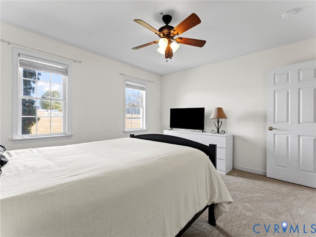 Bedroom with a large white-covered bed, two windows, and a ceiling fan.