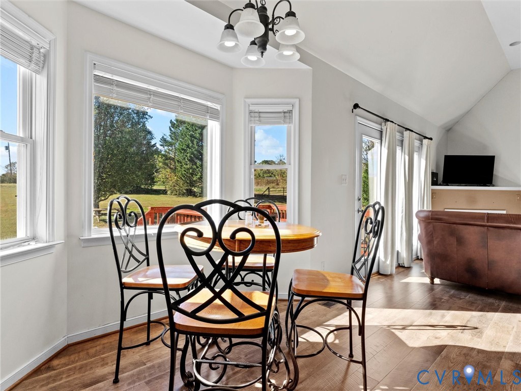 Dining area with a round wooden table and large windows overlooking a green yard.