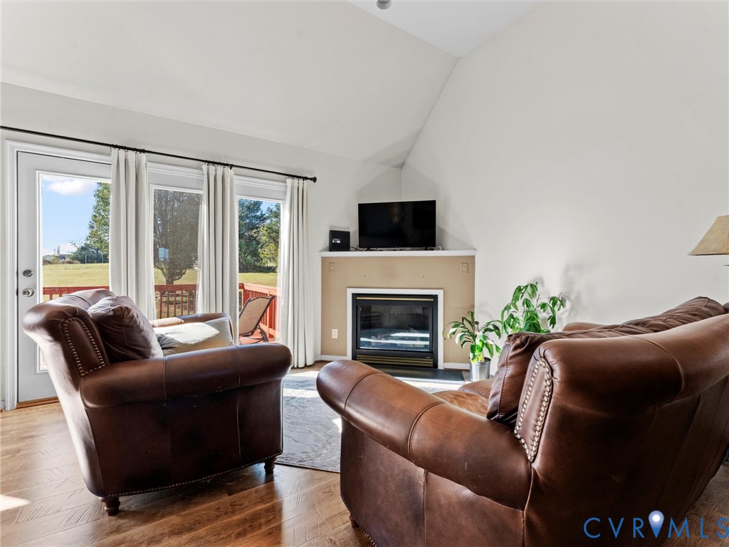 Living room with leather seating, a fireplace, vaulted ceiling, and glass doors opening onto a deck.