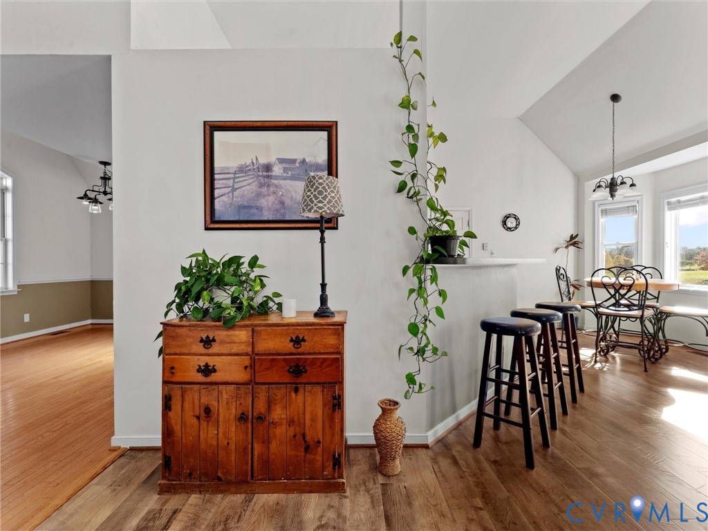 Open dining area with vaulted ceilings, hardwood floors, tall windows, and a breakfast bar with stools.