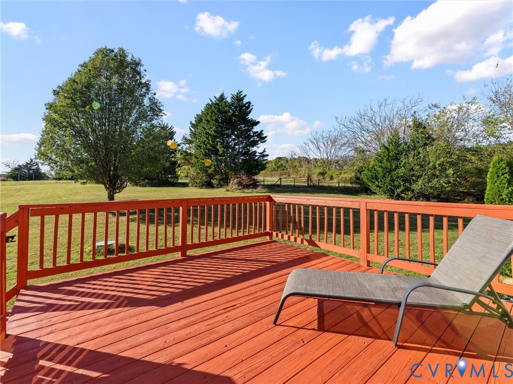 Red wooden deck with lounge chairs overlooking a broad lawn and mature trees.
