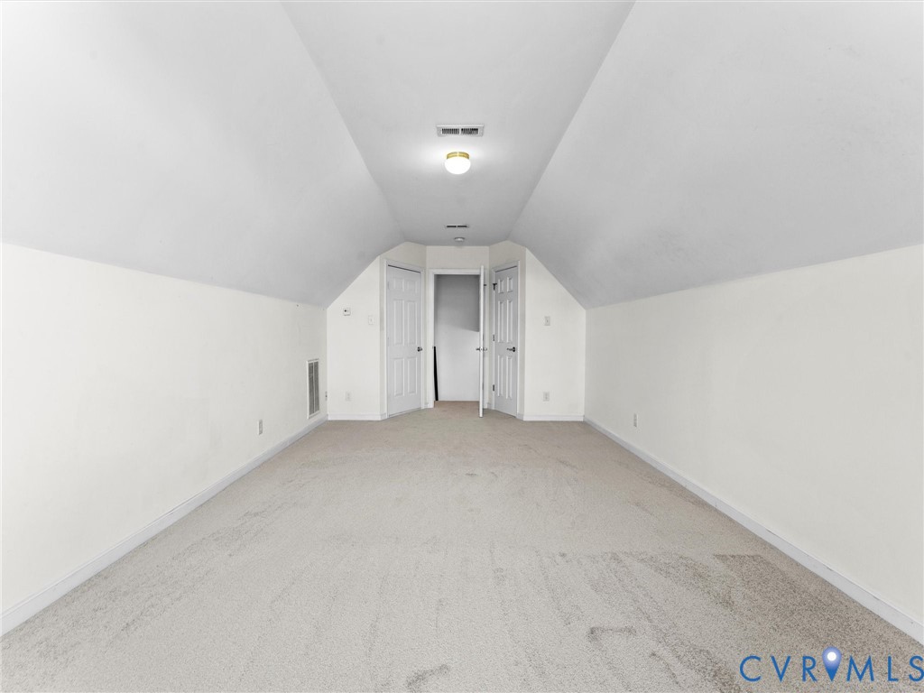 Empty upstairs room with a sloped ceiling, beige carpet, and doors at the far end.