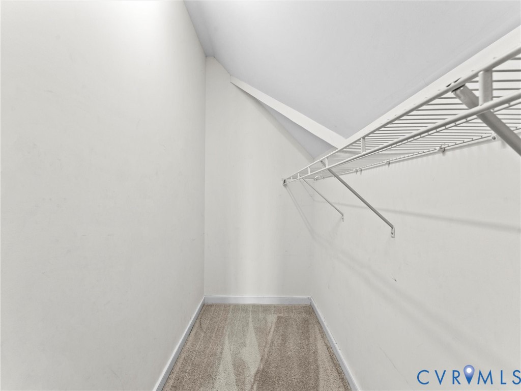 Empty walk-in closet with beige carpet and white wire shelving beneath a sloped ceiling.