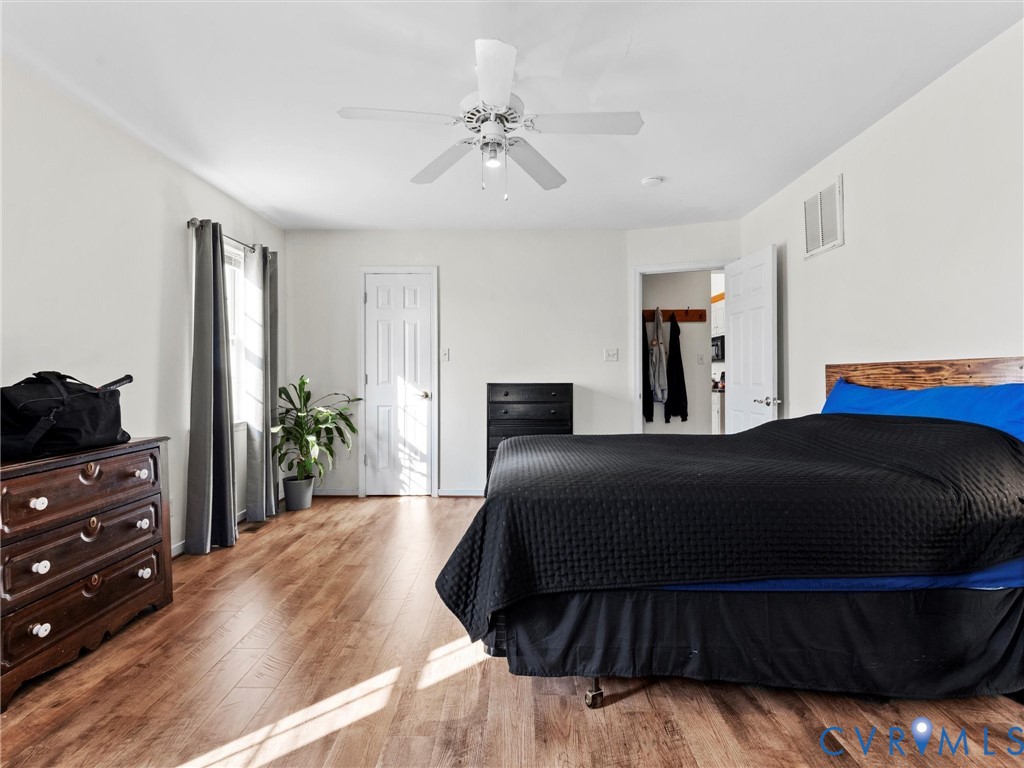 Bedroom with a black-covered bed, hardwood floors, and a ceiling fan.