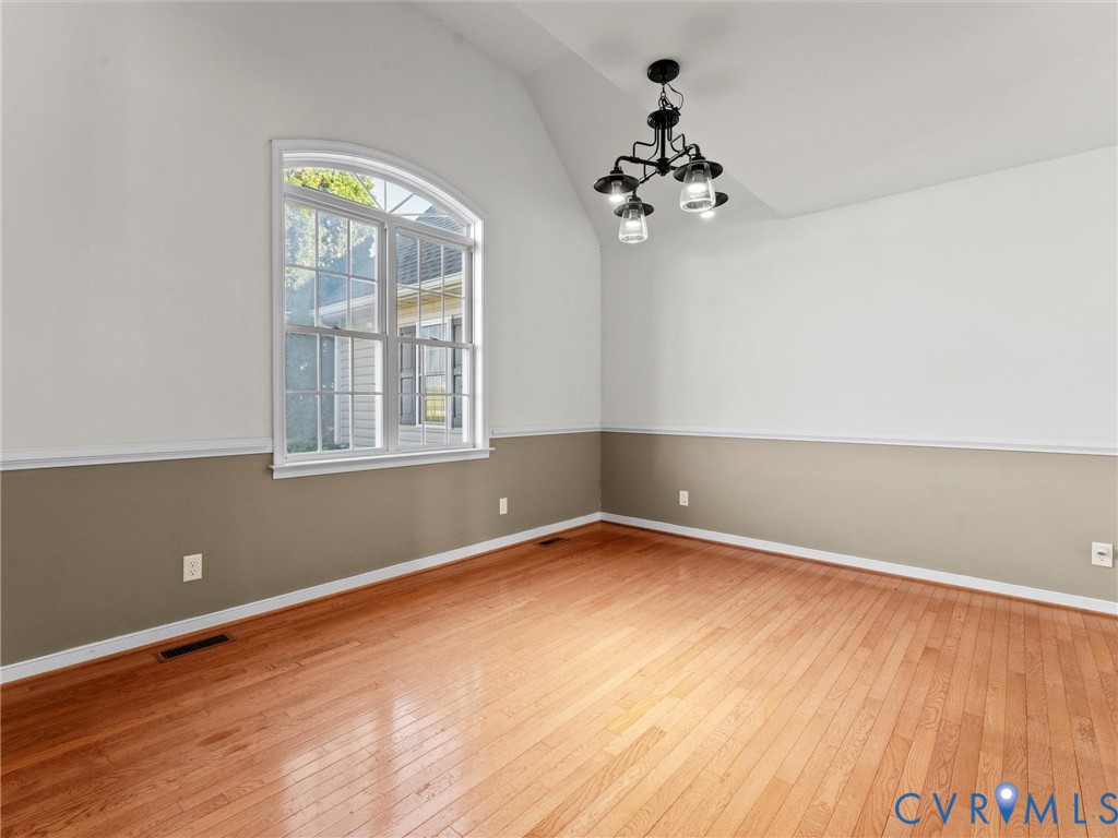 Empty dining room with hardwood floors, an arched window, and a chandelier.