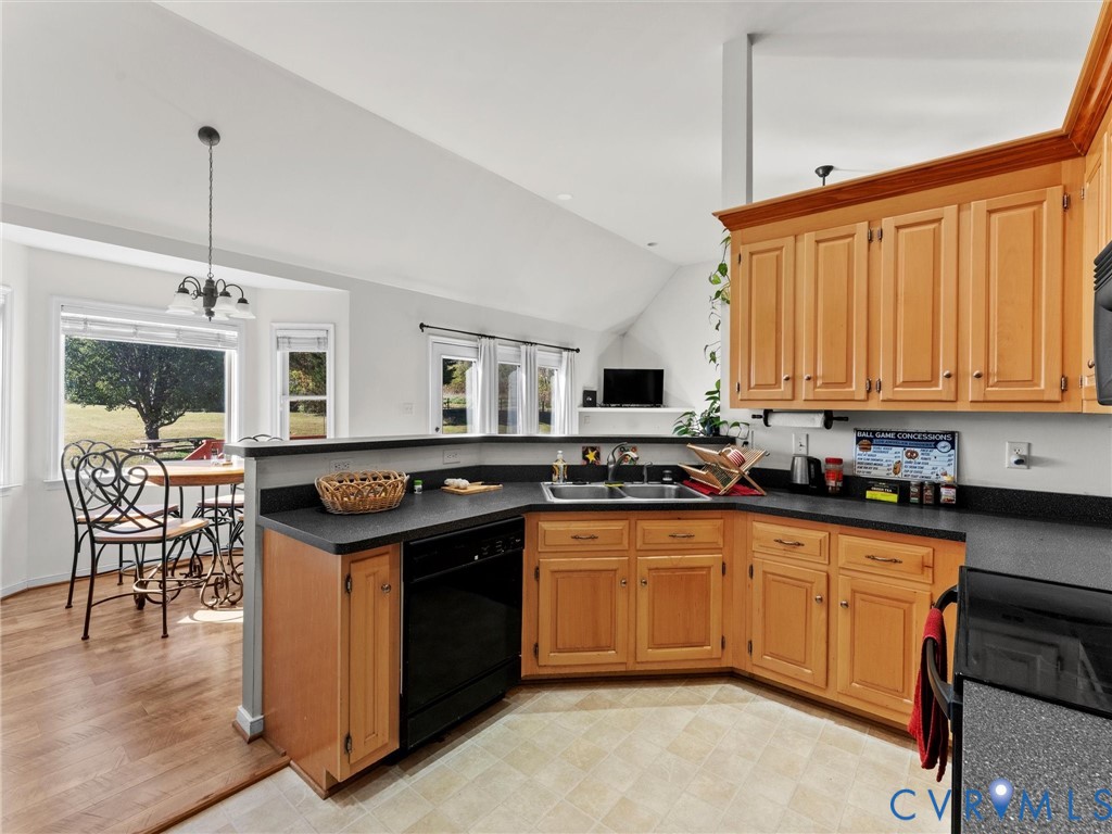 Kitchen with honey-colored cabinets, dark counters, and a dining nook beside large windows.