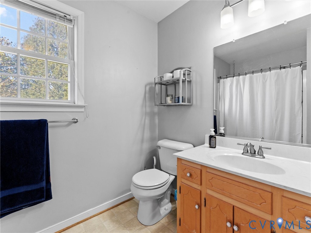Bathroom with a wood vanity, white toilet, curtained tub, and large window.