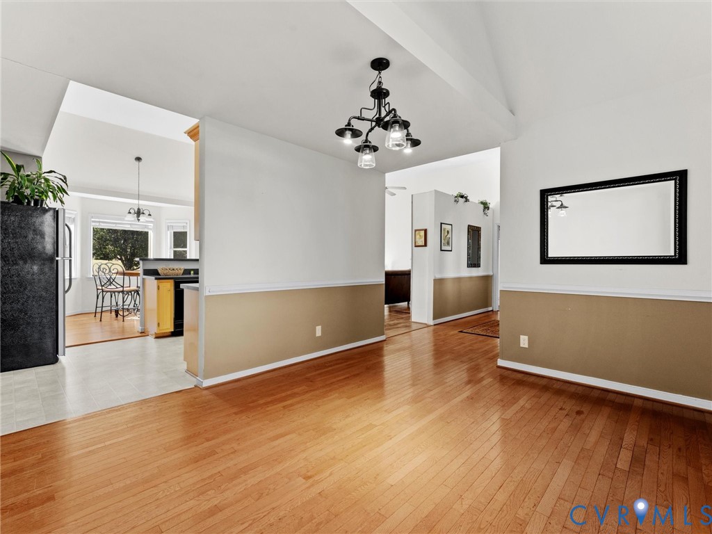 Open dining area with hardwood floors, a black chandelier, and a view into the kitchen and breakfast nook.