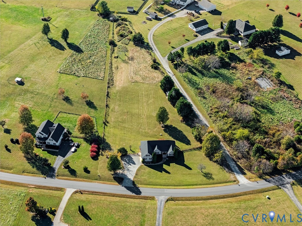 Aerial view of a house on a spacious grassy lot with mature trees and nearby outbuildings.