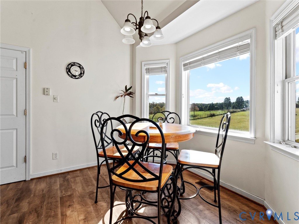 Dining area with a round wooden table and black metal chairs beside windows overlooking open fields.