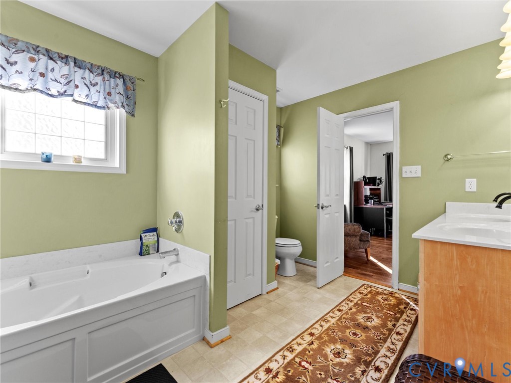Bathroom with a built-in soaking tub beneath a curtained window and a wood-front vanity.