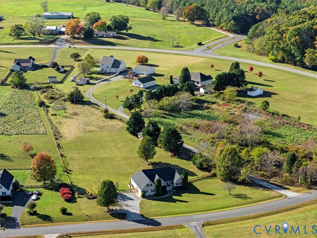 Aerial view of a detached house with a broad lawn, gravel driveway, and surrounding fields.