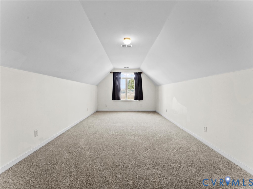 Empty carpeted room with a high sloped ceiling and curtained window.