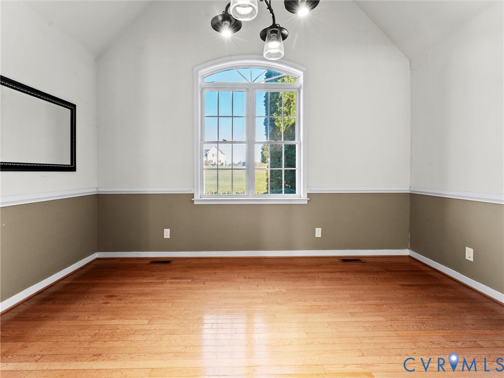 Empty room with hardwood floors, two-tone walls, and a large arched window.