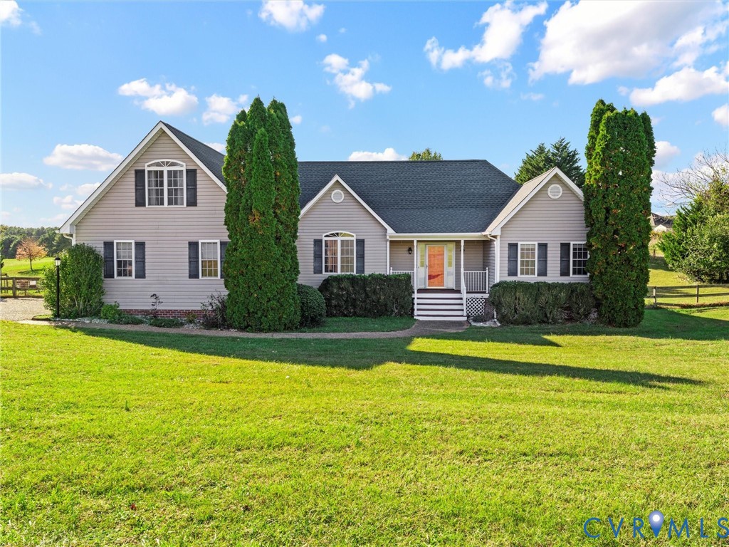 Light-gray home with a covered porch, coral front door, and tall evergreens across the front lawn.