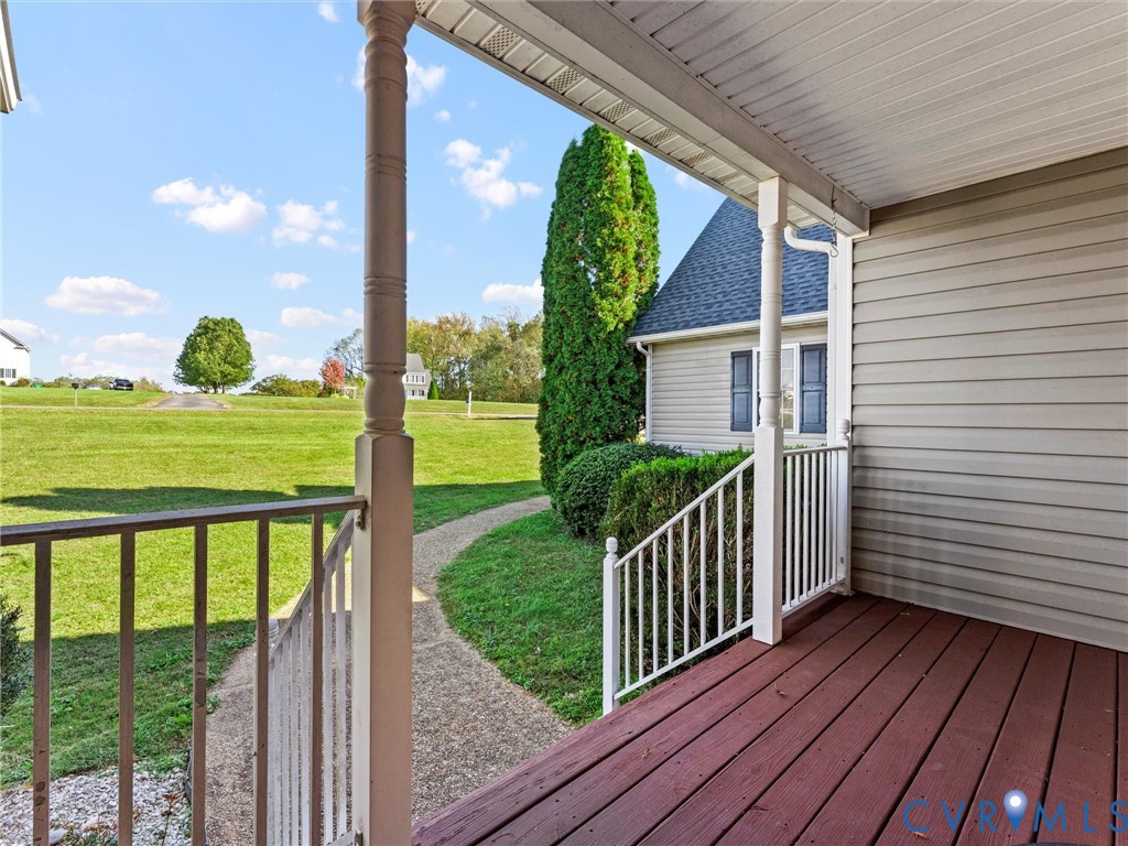 Covered porch with red-brown decking and white railing overlooking a broad lawn.
