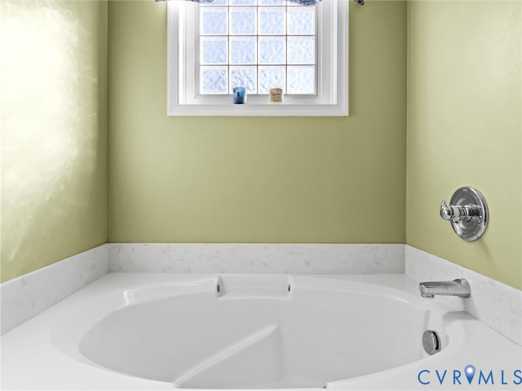 Corner soaking tub beneath a small multi-pane window, with pale green walls and chrome fixtures.