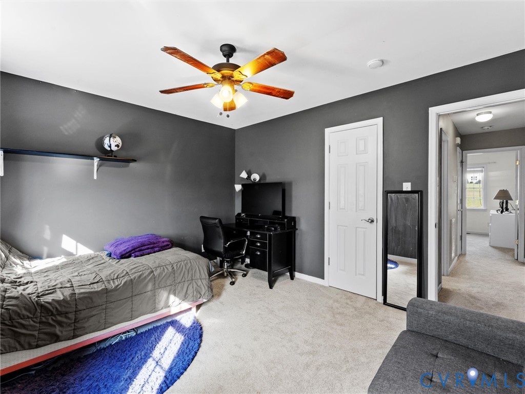 Bedroom with dark gray walls, a gray-quilted bed, desk, full-length mirror, and wooden-blade ceiling fan.