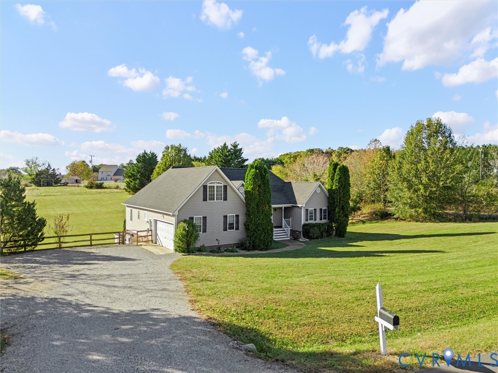 Gray two-story house with attached garage, broad lawn, gravel driveway, and mailbox.