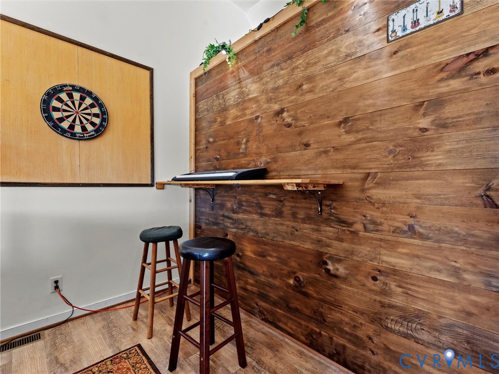 Game room with a dartboard, rustic wood-plank wall, shelf, and two bar stools.